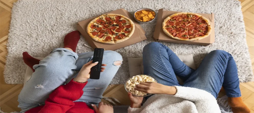 İki kişi pizzalarını ve patlamış mısırlarını hazırlamış ve film izliyorlar.